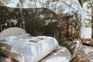 Photograph of a modern bedroom with a clear plastic tent structure and a bed with white bedding.