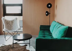 A modern living room features a green velvet sofa, a round coffee table, and a fur-covered chair.