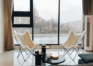 Modern interior living room with white fabric butterfly chairs, black tables, and a scenic view through large windows.