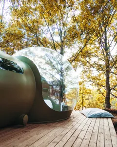 Modern luxury cabin with a glass dome structure and outdoor wooden deck surrounded by autumn trees.
