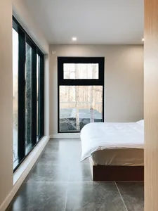 A modern minimalist bedroom featuring a concrete floor, minimalistic furniture, and large windows.