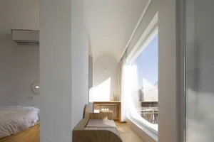 A modern minimalist bedroom with a wooden bench and large window.