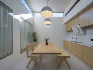 Modern minimalist kitchen with a wooden bench, potted plant, and hanging light fixtures.
