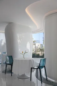 A minimalist restaurant interior with a white tablecloth, glass vase with tulips, and transparent blue plastic chairs.