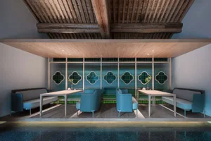 A modern restaurant interior with a wooden floor and ceiling, greenery accents, and blue seating arrangements.