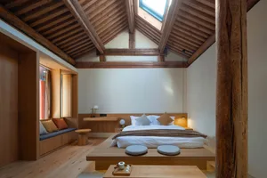 A minimalist bedroom with a wooden bed, light-colored bedding, and a skylight in the ceiling.
