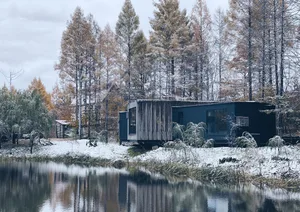 A modern, ultra-modern residential building surrounded by a snowy landscape with a serene lake reflecting the scene.