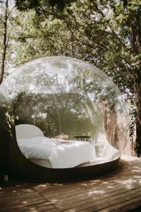 Transparent bubble-shaped outdoor bedroom with a white bed and minimalistic design.