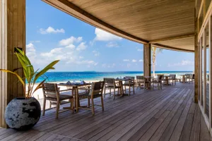 A wooden patio overlooking the ocean with tables and chairs.