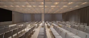 Multiple rows of fabric-covered chairs arranged in a spacious conference room with a minimalist design.