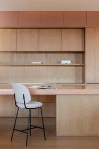 A modern desk with a terrazzo countertop and a cushioned stool in front of wooden cabinets.