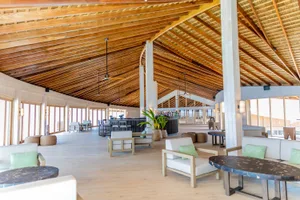 Modern hotel lobby with white and green furniture, wooden ceiling beams, and a bar area.