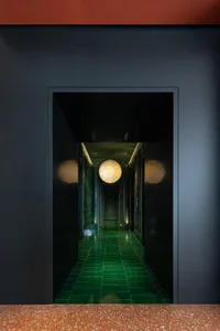 A minimalist glass corridor with green tiles and spherical lights.