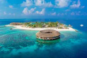 Aerial view of a resort island with a circular thatched-roof building and a white sandy shore.