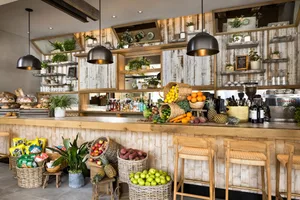 A cozy coffee shop with wooden decor and a variety of fruits displayed in baskets on the counter.
