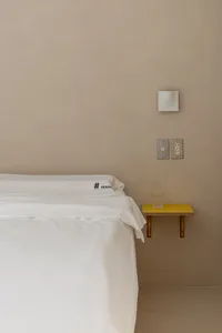 A minimalist bedroom with white textiles on a concrete wall.