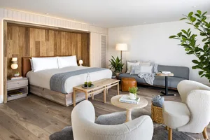 A minimalist hotel suite featuring a wooden bed and furniture.