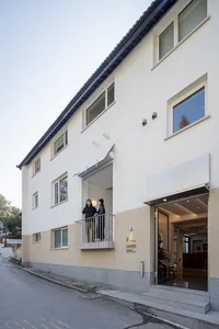 Modern building with concrete exterior features a balcony and large windows.