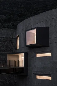 Modern building exterior with concrete walls, illuminated windows, and balconies.