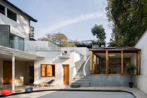 A modern residential exterior featuring a white concrete facade with large windows and some greenery.