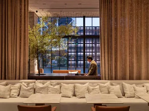 A modern restaurant interior with a long bench, leather couches, and fabric curtains.