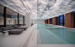 A modern indoor swimming pool with glass walls and a futuristic ceiling.