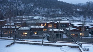 A modern residential architecture nestled in a snowy valley with stone and glass materials.