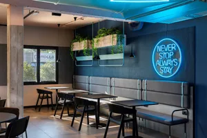 Modern interior design of a cafe featuring concrete walls and floors, with seating arrangements, pendant lights, and potted p