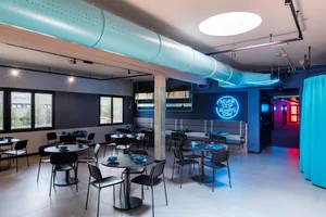A modern industrial cafeteria interior with concrete walls, steel beams, and large windows.
