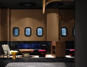 A modern hotel lobby featuring a black leather sofa with blue pillows, a wooden coffee table, and a metal lamp on a wooden fl