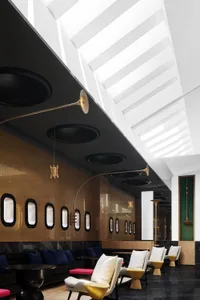 A modern hotel lobby features sleek furniture, glass walls, and a high ceiling with skylights.