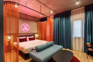 Modern hotel room with a bed, curtains, and a sign that says 'Let's Stay in Bed'.