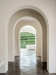 Modern minimalist bathroom featuring a white bathtub on a polished concrete floor, framed by arches of plaster and viewed thr