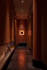 A minimalist corridor with concrete flooring and walls, lit by recessed lighting.