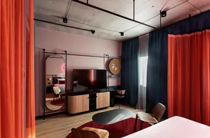 A modern minimalist hotel bedroom suite featuring a large bed, a flat-screen TV, and a comfortable seating area with wooden f