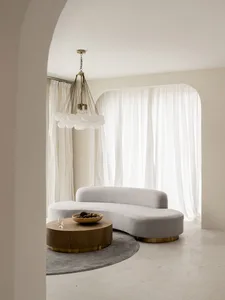 A modern, neutral-toned living room with a curved sofa, round coffee table, and chandelier.