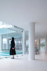 A modern interior design featuring a glass-walled lounge area with a poolside view, using concrete and glass materials.