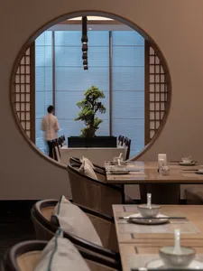 現代餐廳室內空間，擺設木質桌椅、圓形窗戶與盆栽。