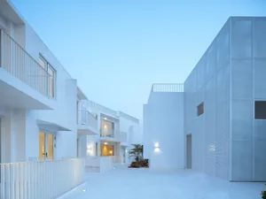 White concrete exterior of a modern building with balconies and lighting fixtures.