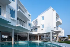 A modern, white-rendered concrete exterior of a residential house with a swimming pool and outdoor seating area.