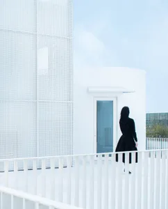 A modern building with a white perforated metal facade and a white concrete entrance.