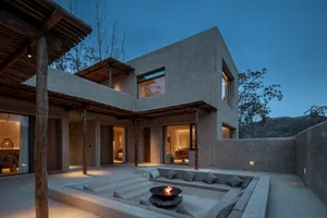 A modern concrete lounge area with a fire pit and comfortable seating.