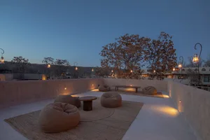 Concrete outdoor lounge area with bean bag chairs and wooden table, illuminated by lanterns.