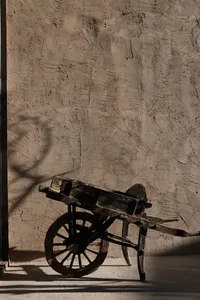 A rustic wooden wheelbarrow leaning against a textured concrete wall.