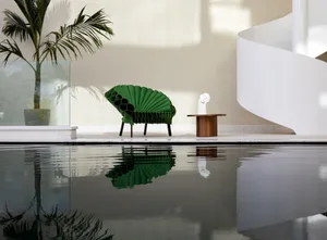 A stylish industrial interior design featuring a green fabric armchair and a white sculpture on a bronze pedestal reflected i