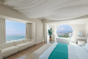 Modern minimalist hotel room with white decor and a view of the ocean.