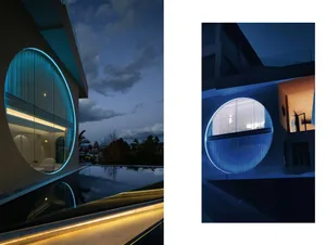 A modern house with a circular window illuminated by blue lighting at dusk.