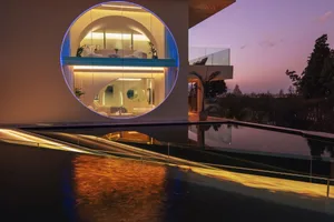 Modern house exterior with glass and concrete materials, illuminated during sunset.