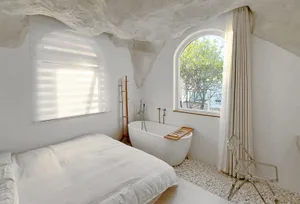 A minimalist bedroom with a concrete ceiling, white bedding, and a freestanding bathtub.