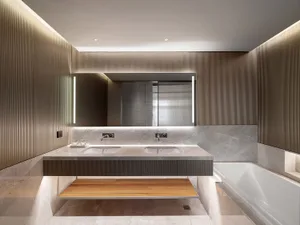 A modern bathroom features a marble vanity with concrete accents and a wooden shelf beneath it, illuminated by soft lighting.